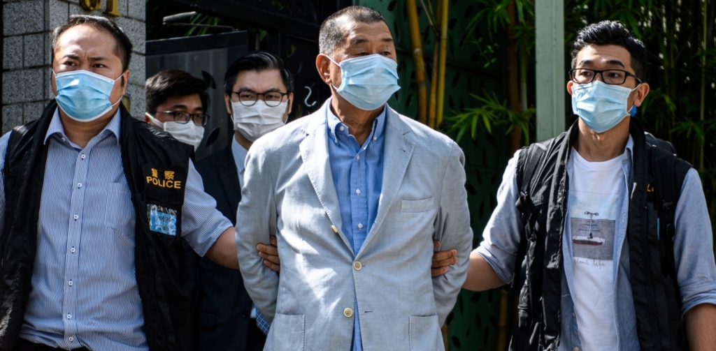 Man in a pale suit, flanked by police officers.